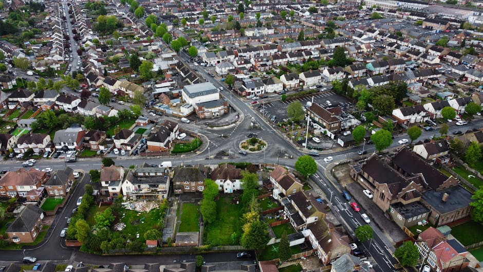 An aerial view of a residential neighbourhood showing a row of terraced houses with small private gardens, backyards, and parked cars along the driveways. The scene includes a mix of detached and semi